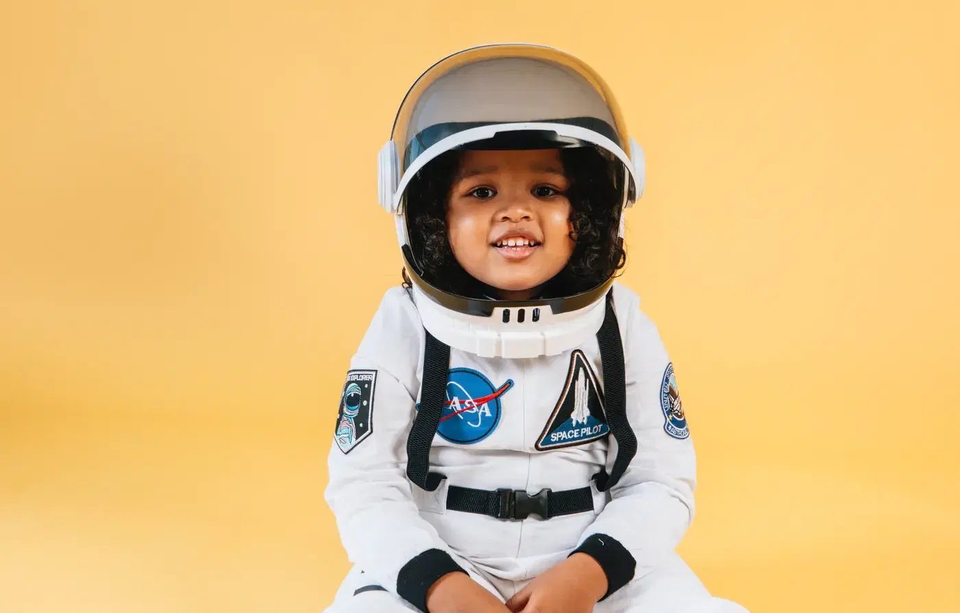 A small child in a toy astronaut suit and helmet on a yellow background